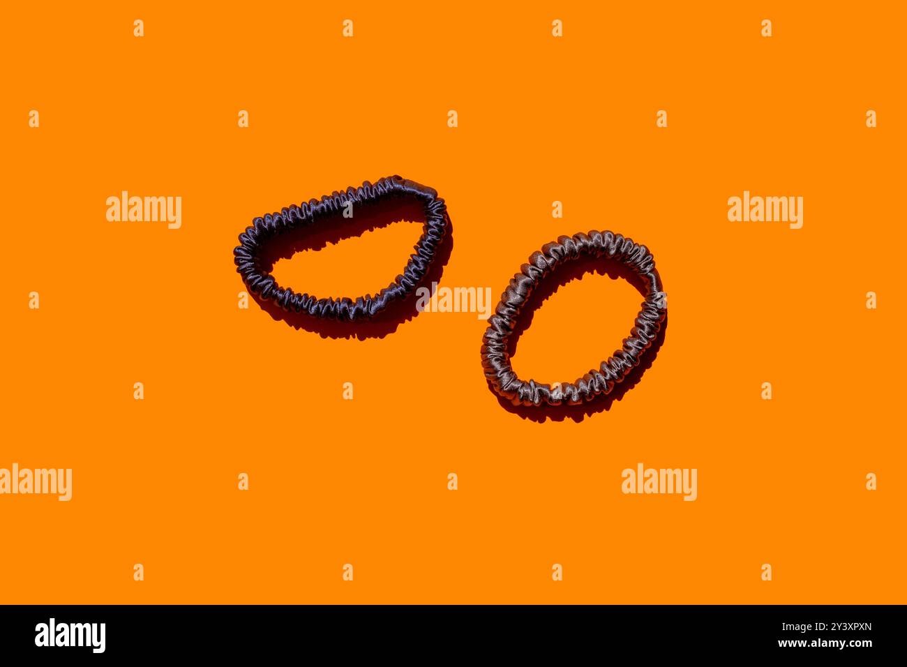 Zwei Seidenhaar-Scrunchies für Mädchen und Frauen auf orangefarbenem Hintergrund, perfekt für die Werbung für Haaraccessoires, Schönheitsprodukte oder Modetrends. Ideal für Stockfoto