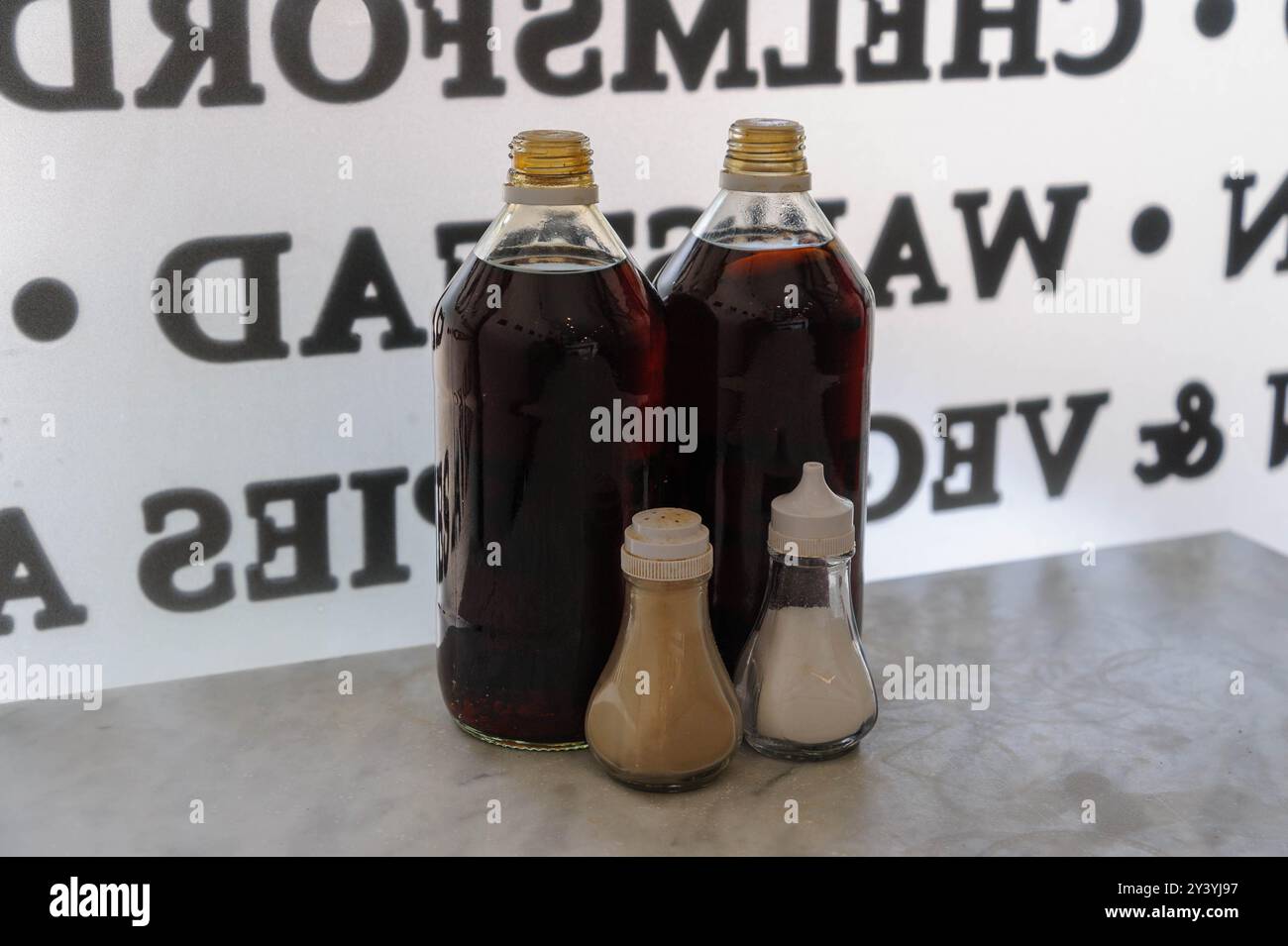 Essig-, Salz- und Pfefferflaschen auf einem Tisch vor einem Café-Fenster mit umgekehrter Schrift. Stockfoto