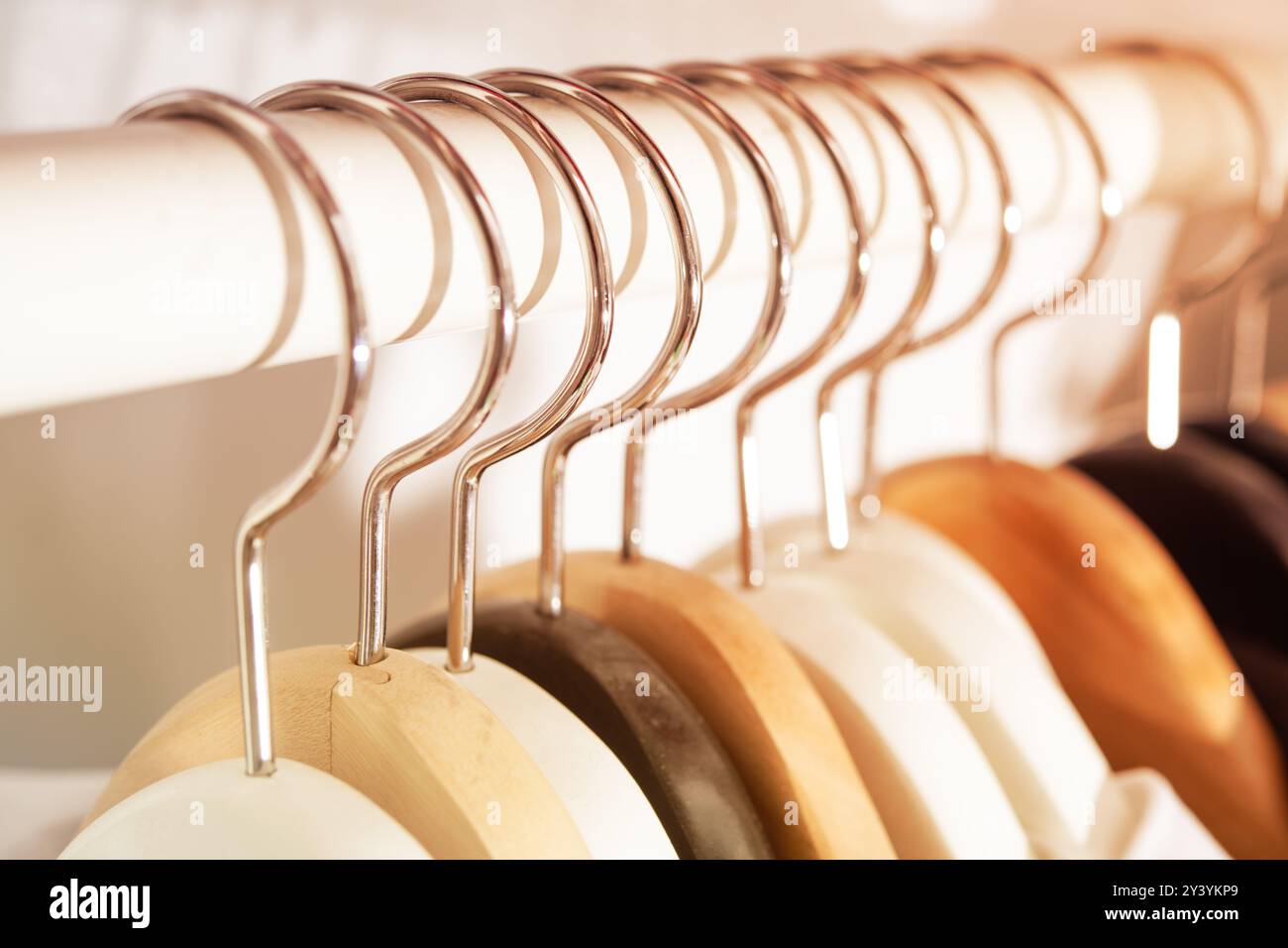 Aus nächster Nähe sehen Sie hölzerne Kleiderbügel in verschiedenen Farben, die ordentlich auf einem weißen Regal hängen und die Organisation und Ästhetik in Modeaufbewahrung und -Clo symbolisieren Stockfoto