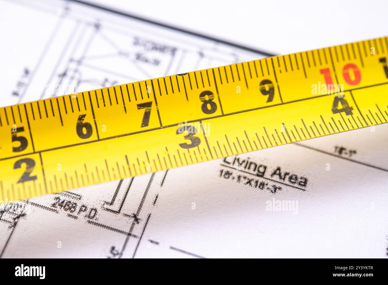 Ein gelbes Maßband, das über detaillierten Architekturplänen positioniert ist und präzise Maße für Wohnraumabmessungen angibt und die Impo unterstreicht Stockfoto