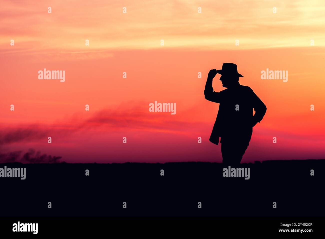 Silhouette eines männlichen Landwirts mit Strohhut, der im Sommer Sonnenuntergang auf dem Feld steht, mit Himmel als Kopierraum Stockfoto