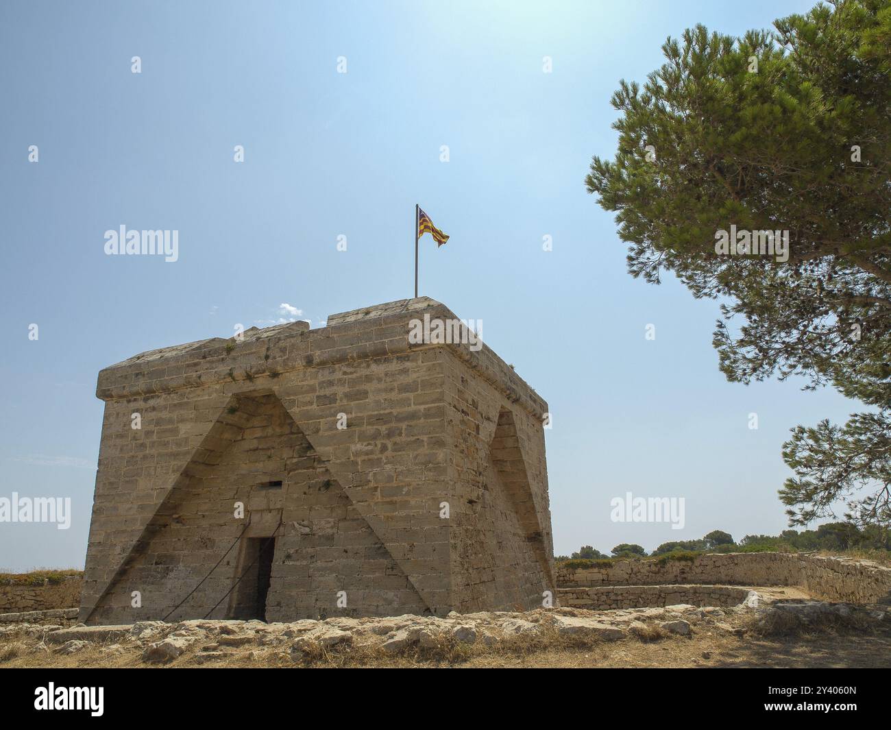 Steingebäude mit einer Flagge auf dem Dach, umgeben von Natur unter hellblauem Himmel, sa Coma, mallorca, spanien Stockfoto