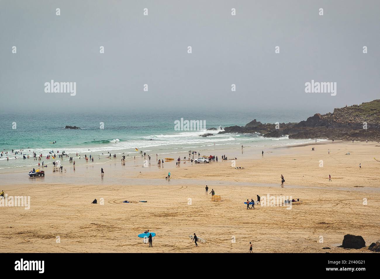 Eine bewölkte Strandszene mit Leuten, die verschiedene Aktivitäten genießen. Das Sandstrand ist gespickt mit Strandgängern, einige schwimmen im Meer, andere entspannen sich Stockfoto