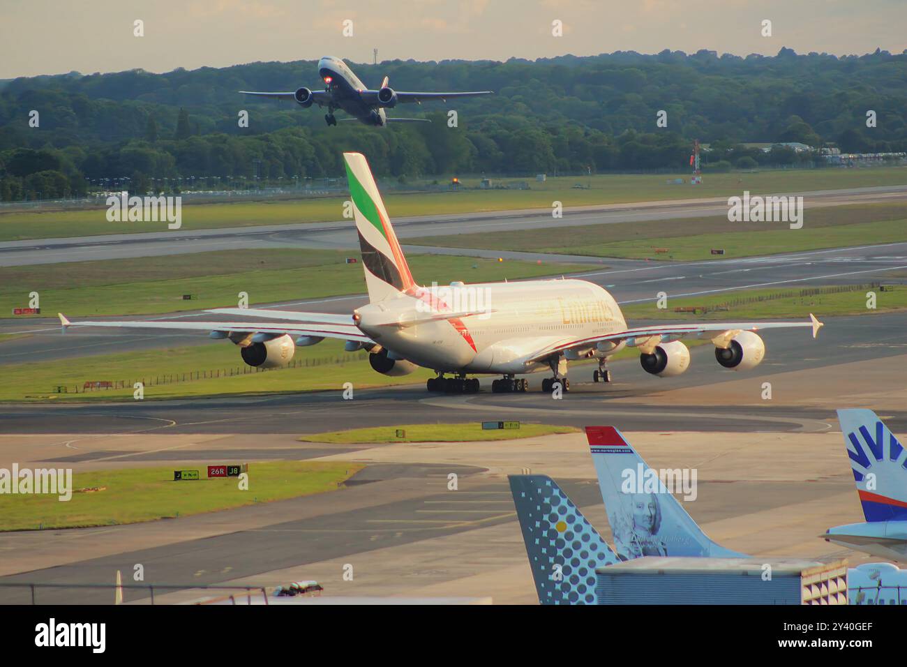 Nach der Landung am Flughafen Gatwick fährt eine Emirates A380 mit dem Taxi, während eine British Airways Boeing 777 im Hintergrund von der Start- und Landebahn abhebt. Stockfoto