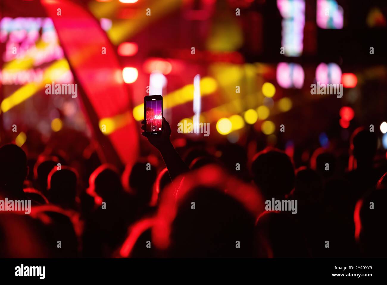 Bühnenlichter als Unschärfe-Bokeh-Hintergrund bei einem Musikkonzert und Hand mit Smartphone-Video, das die Live-Show aufzeichnet Stockfoto