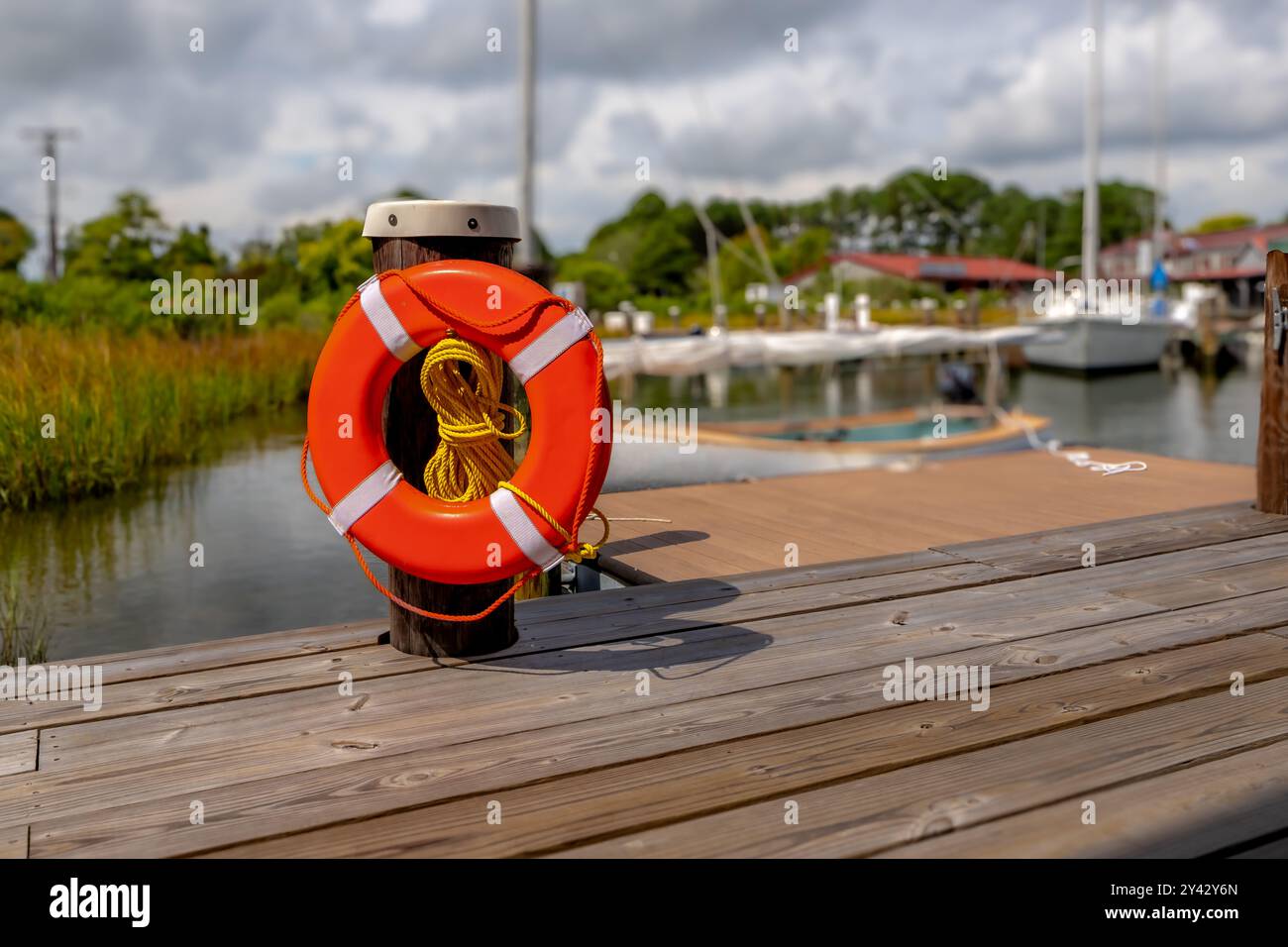 Orangefarbener Rettungsring, Hafenlebensretter, montiert auf einem Dockenstapel mit einem gelben Nylonseil. Stockfoto