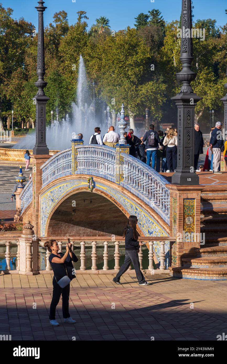 Sevilla, Spanien - 24. Oktober 2023: Menschen an der Plaza de Espana mit Brücke über Kanal und Brunnen im Maria Luisa Park, Wahrzeichen der Stadt. Stockfoto