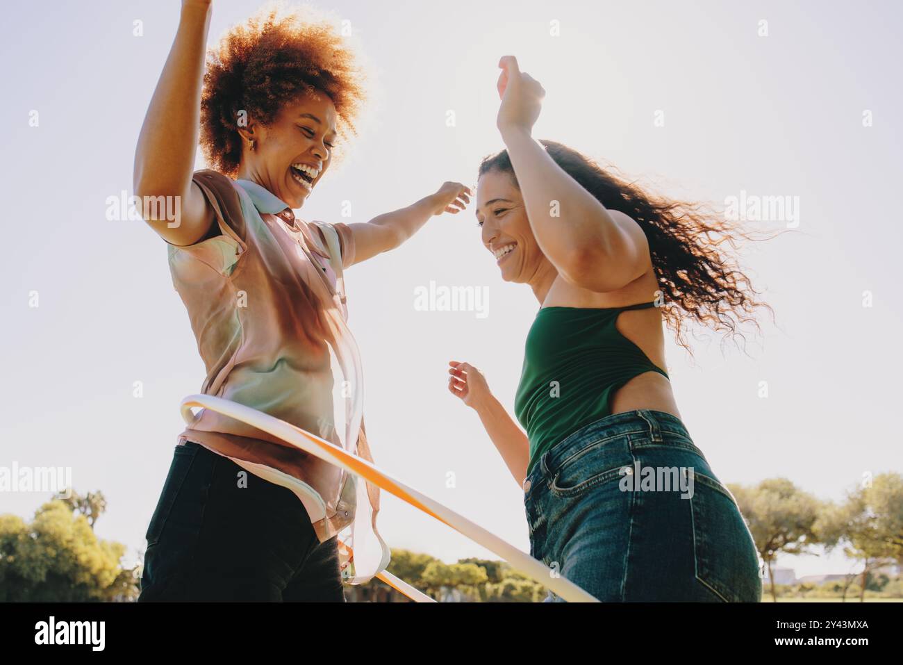 Zwei Freunde genießen an einem sonnigen Tag im Park lustige Aktivitäten mit Hula Hoop. Ein fröhlicher Outdoor-Moment. Stockfoto