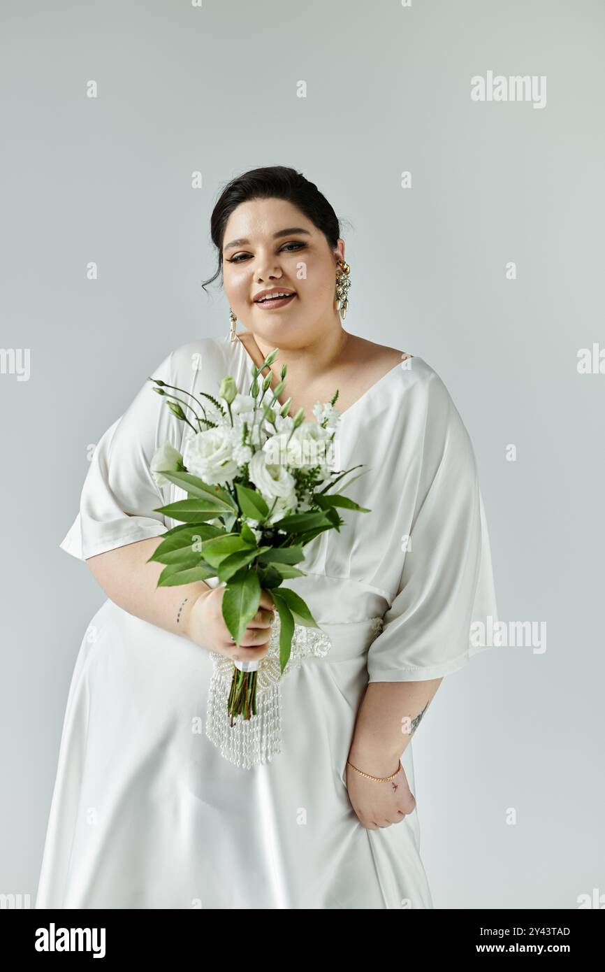 Eine strahlende Braut in Übergröße in einem atemberaubenden weißen Kleid hält einen wunderschönen Blumenstrauß und strahlt Freude und Selbstvertrauen aus. Stockfoto