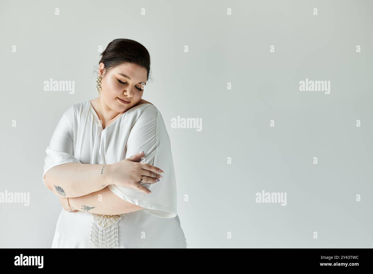 Eine reizende Braut in einem weißen Kleid umarmt sich und zeigt ihre Eleganz und Anmut in einer ruhigen Umgebung. Stockfoto