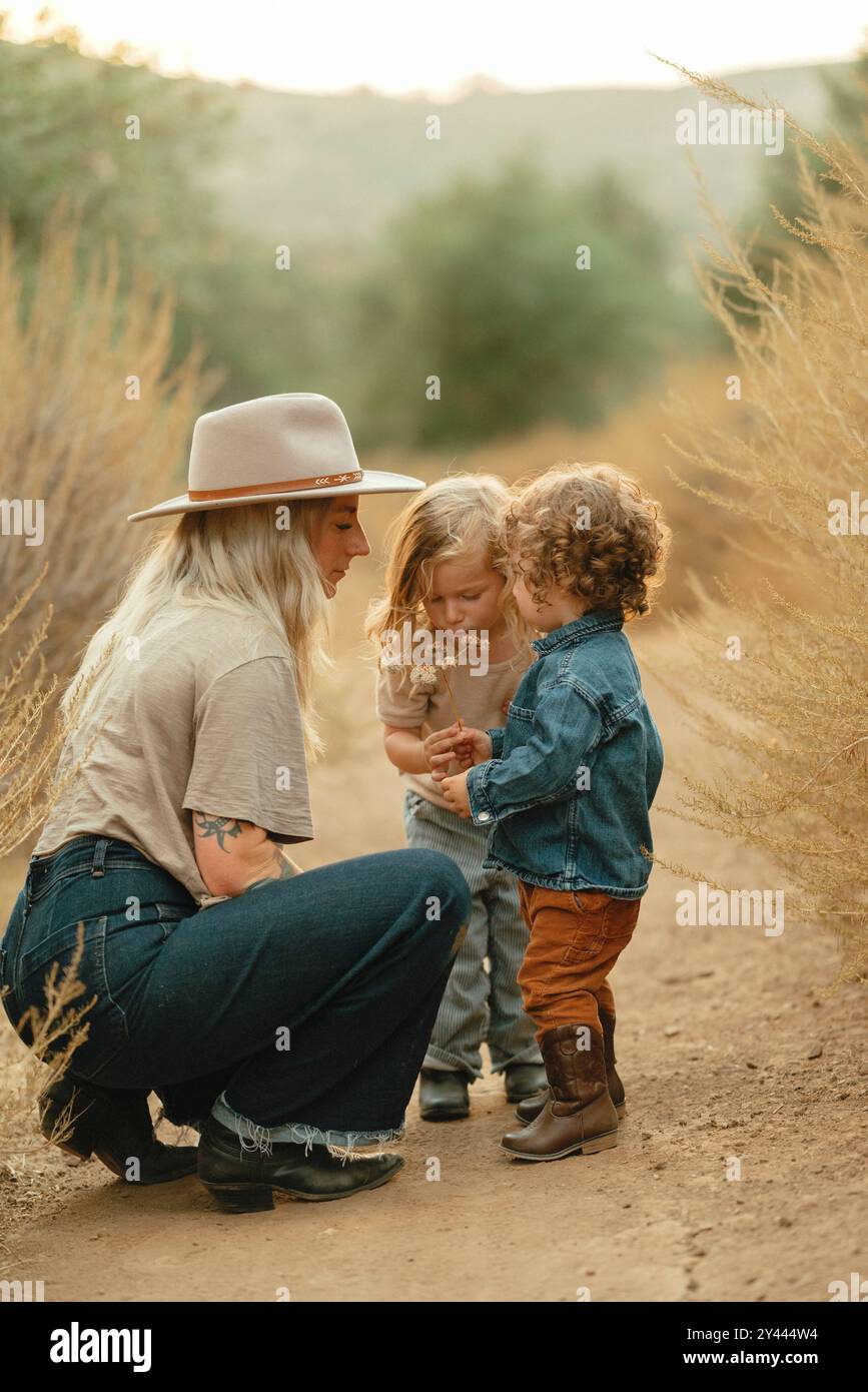 Eine Mutter und zwei Kinder sehen sich Blumen auf einem Weg an Stockfoto