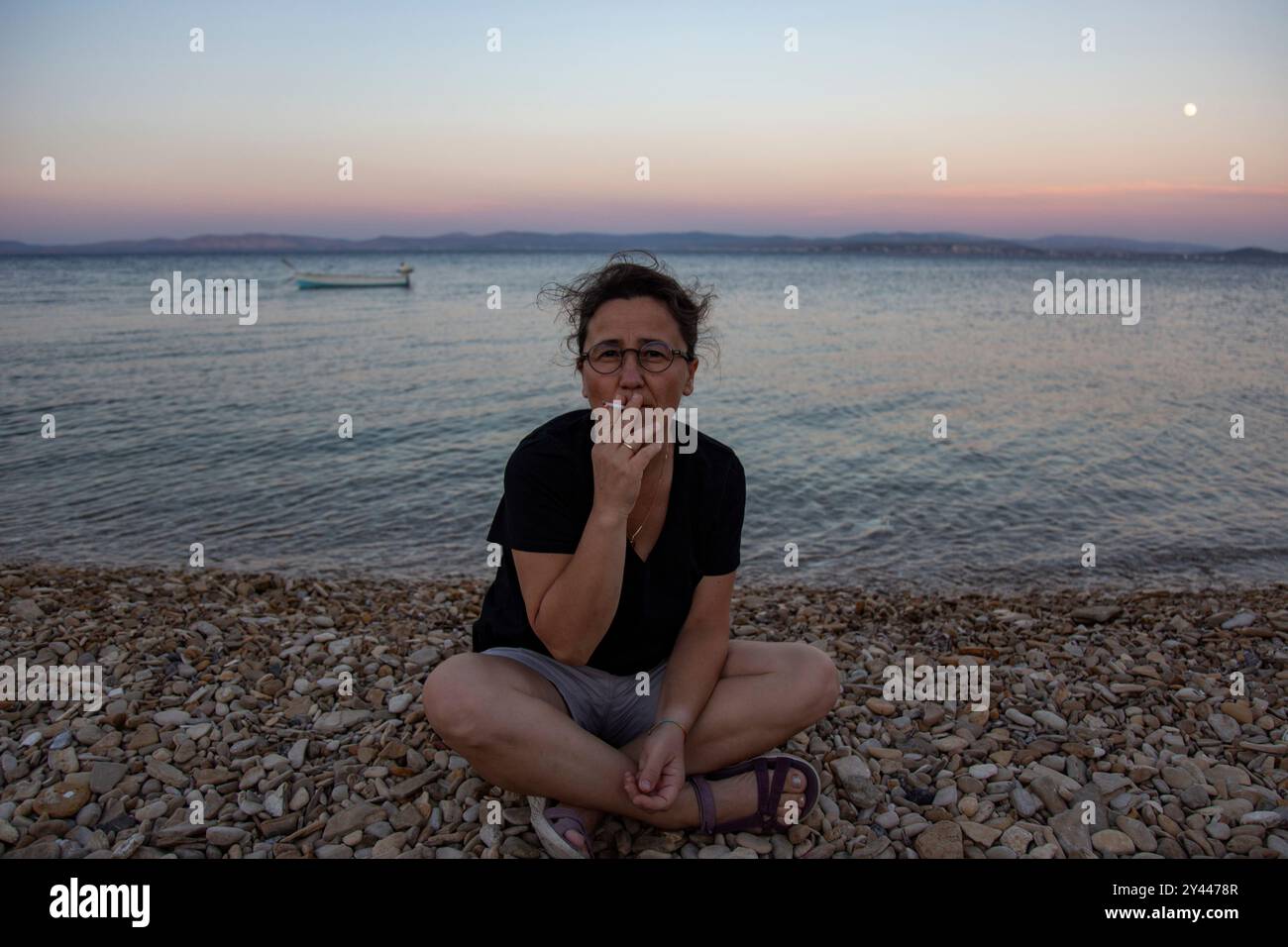 Reife Frau mit Brille raucht am Strand bei Sonnenuntergang Stockfoto