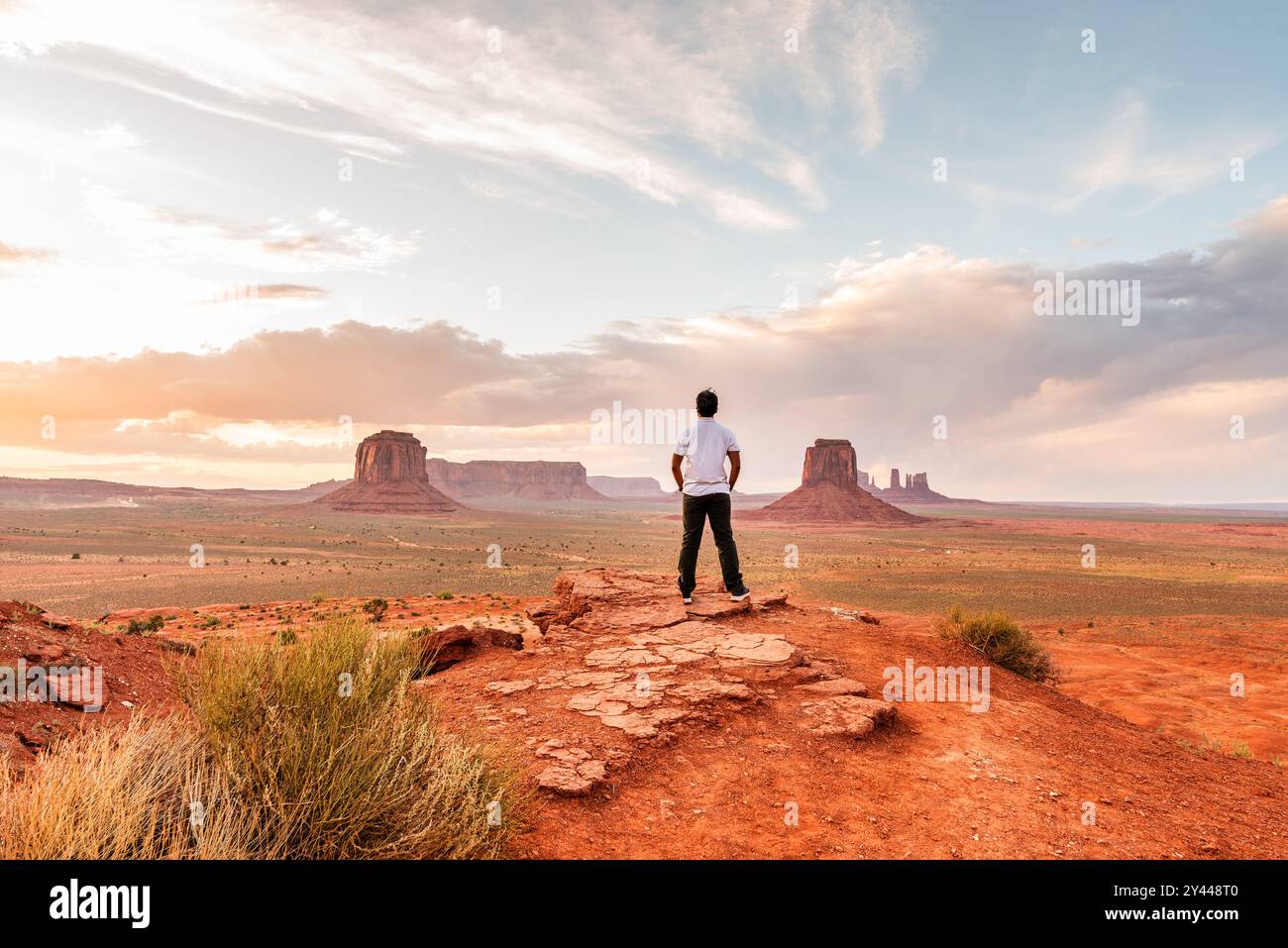 Mann, der auf einem Felsvorsprung steht und das Monument Valley bei Sonnenuntergang überblickt. Stockfoto