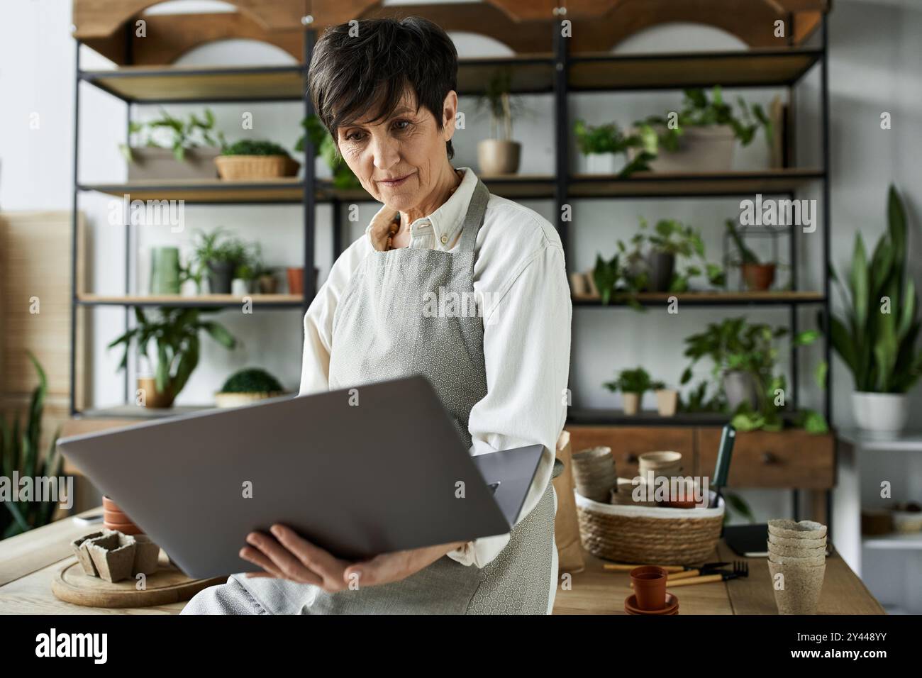 Eine Frau kümmert sich um ihre Pflanzen und arbeitet an ihrem Laptop in ihrem Studio. Stockfoto