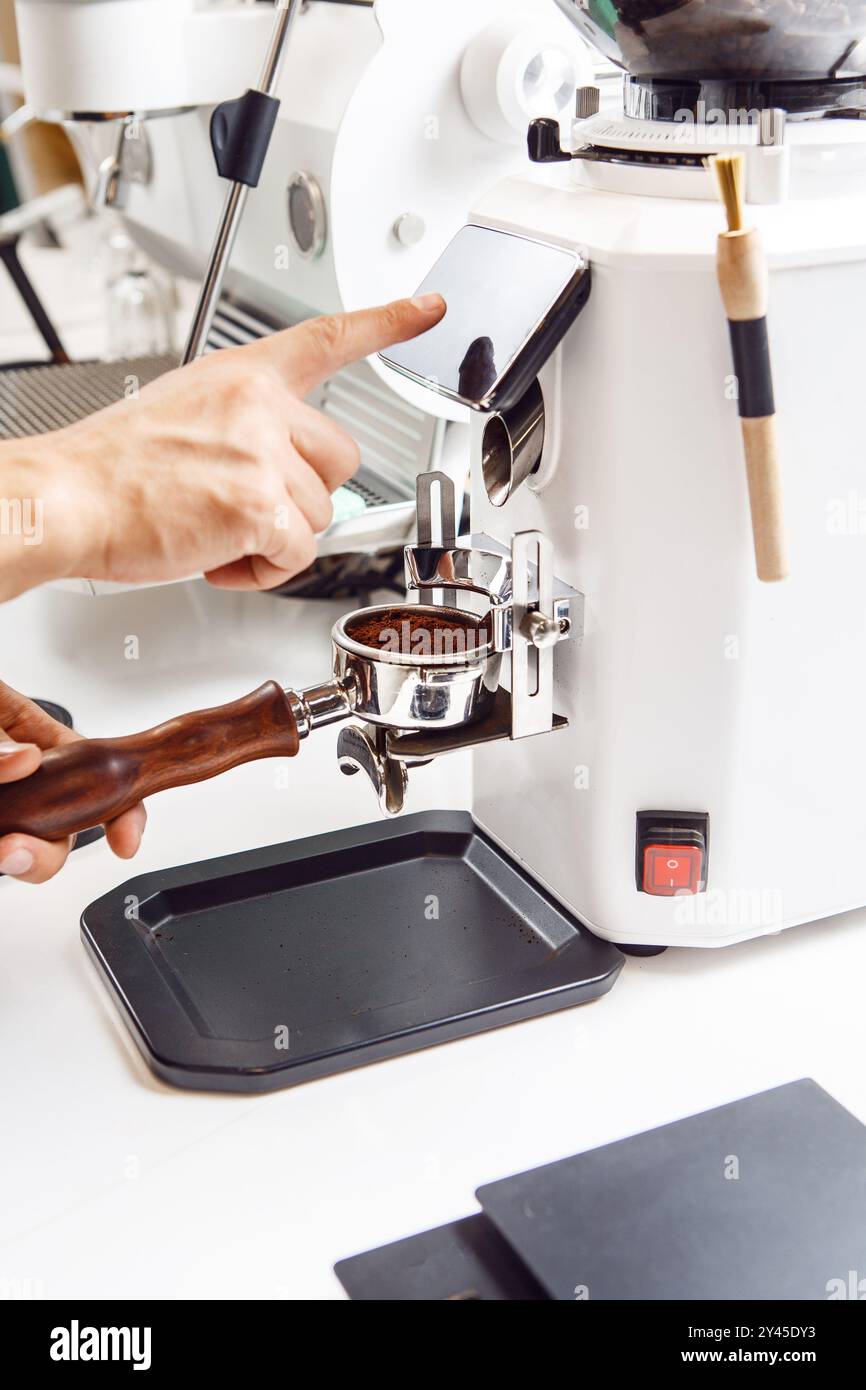 Der gesichtslose Barista stellt das Gewicht für das Einfüllen von Kaffee mit einem Grinder in den Portafilter für die Zubereitung von Espresso sorgfältig ein Stockfoto