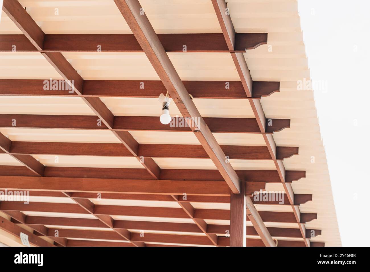 Aus nächster Nähe eine Holzdeckenkonstruktion mit freiliegenden Balken und einer einzelnen Glühbirne. Die Decke ist mit einer Kombination aus Holz ausgestattet Stockfoto