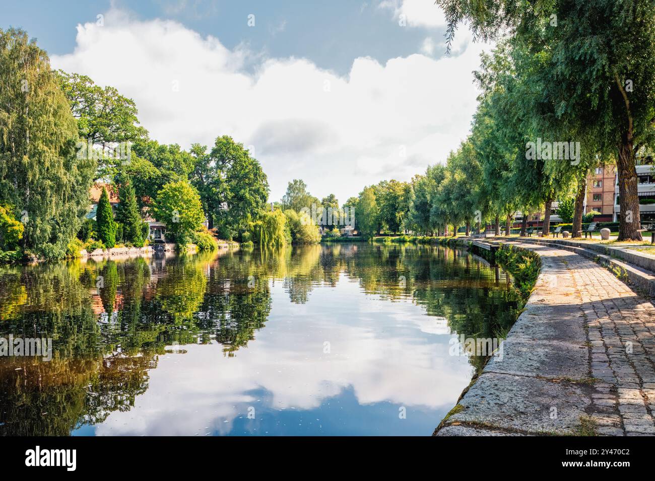 Blick auf einen üppigen Flussweg im Stadtpark mit hohen Bäumen und Reflexionen im Fluss Svartån. Entspannung und urbanes Entspannungskonzept. Orebro, Schweden. Stockfoto