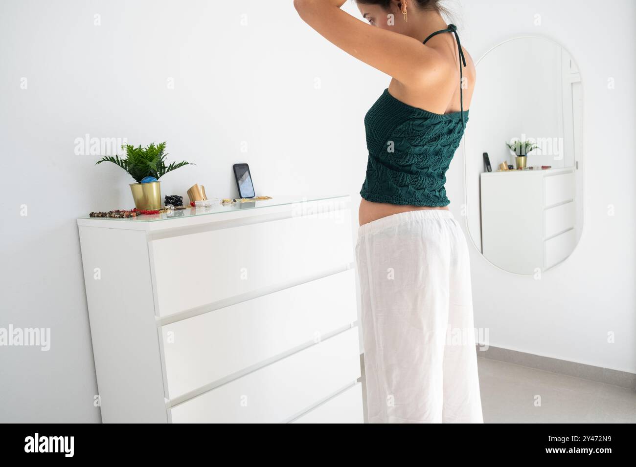 Eine junge Teenagerin bereitet ihre Frisur vor ihrem Smartphone vor, während sie eine Geschichte oder eine Rolle für soziale Netzwerke macht. Weißes Tageszimmer und zwangloses Ambiente Stockfoto