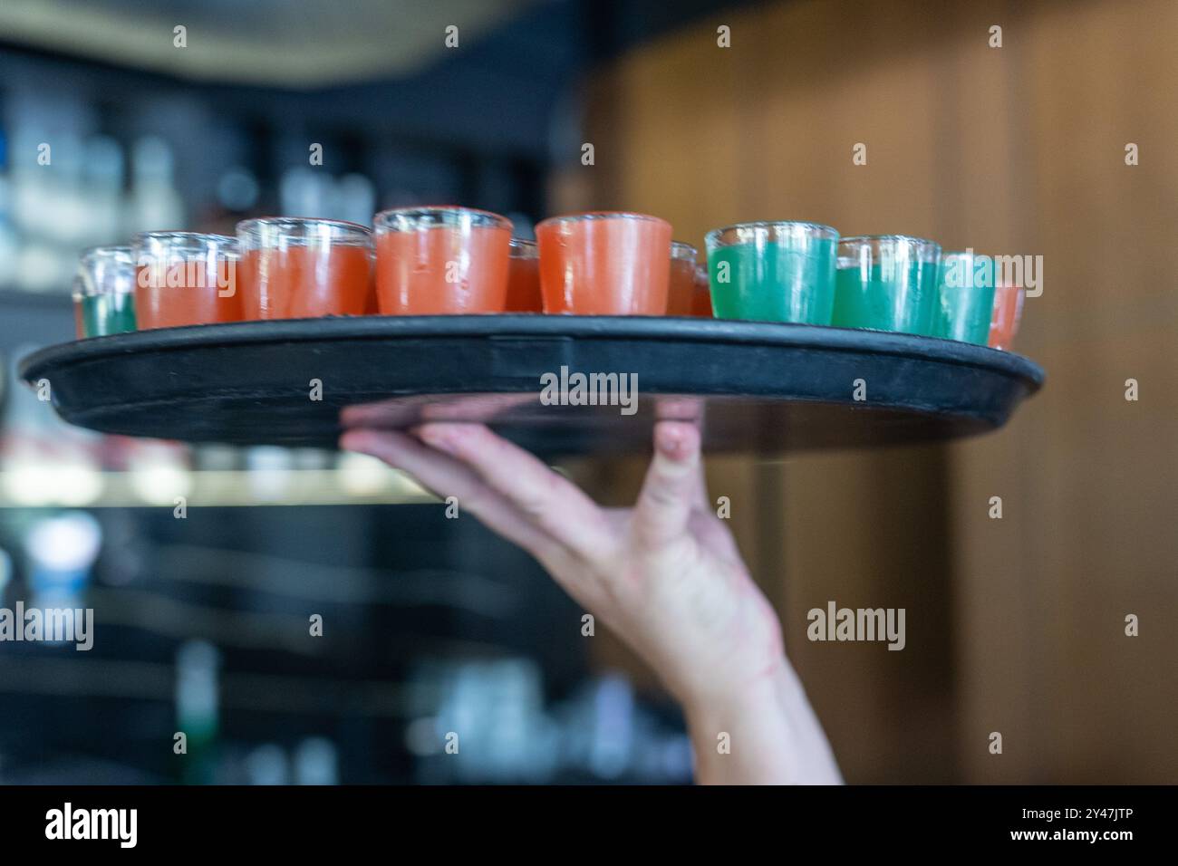 Party Booster Shots: Leuchtende Orange- und grüne Getränke auf schwarzem Tablett, verschwommener Hintergrund. Stockfoto