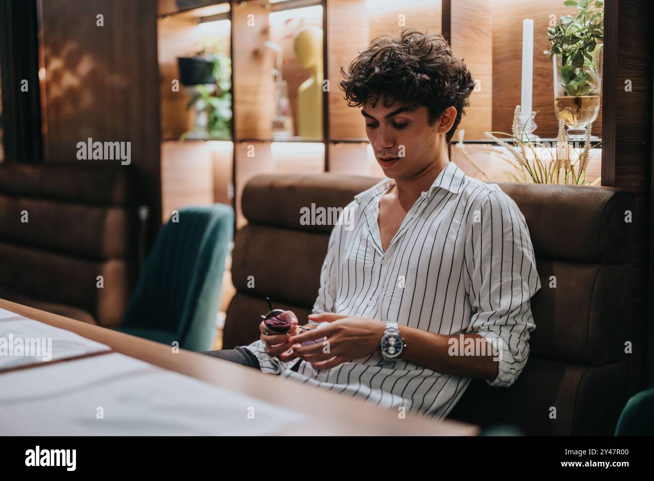 Der junge Mann sitzt allein in einem Restaurant und wartet geduldig auf sein Date. Die Atmosphäre ist modern und einladend, was Vorfreude und Hoffnung suggeriert. Stockfoto