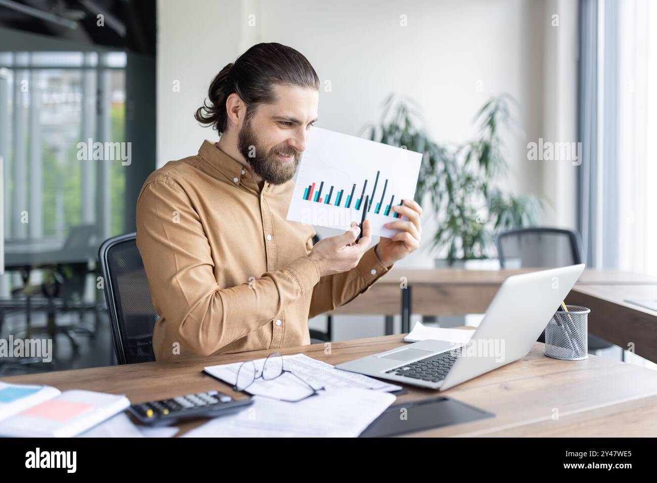Lächelnder Profi präsentiert Wachstumsdiagramme während der Videokonferenz. Erklären Sie den finanziellen Erfolg, indem Sie ein Notebook als visuelle Hilfe verwenden. Die Arbeitsplatzumgebung legt nahe, sich auf die Produktivität des Unternehmens zu konzentrieren. Stockfoto