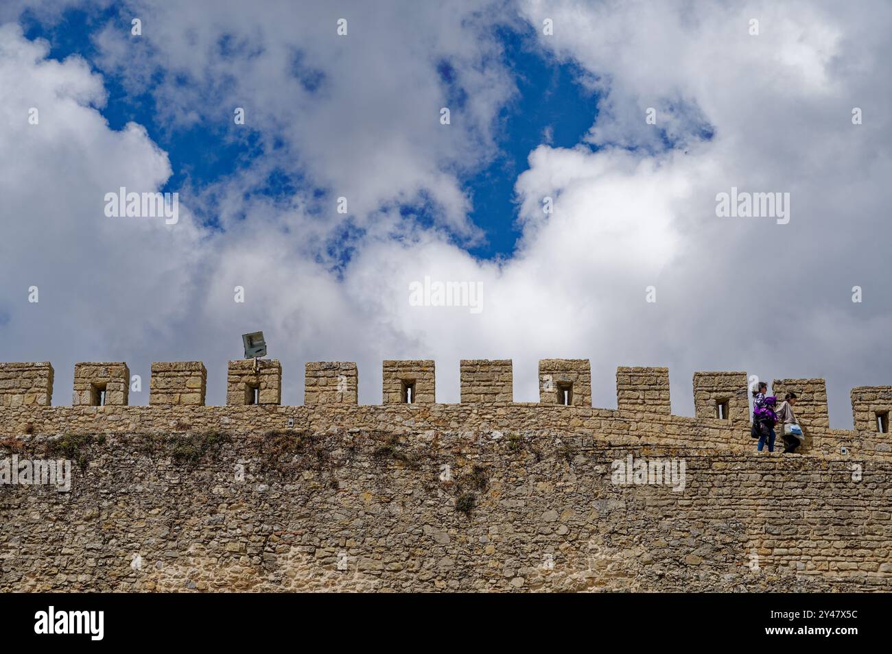 Reisende auf den majestätischen mittelalterlichen Mauern von Óbidos, die alte Steinbefestigungen mit einem dynamischen Himmel verbinden Stockfoto