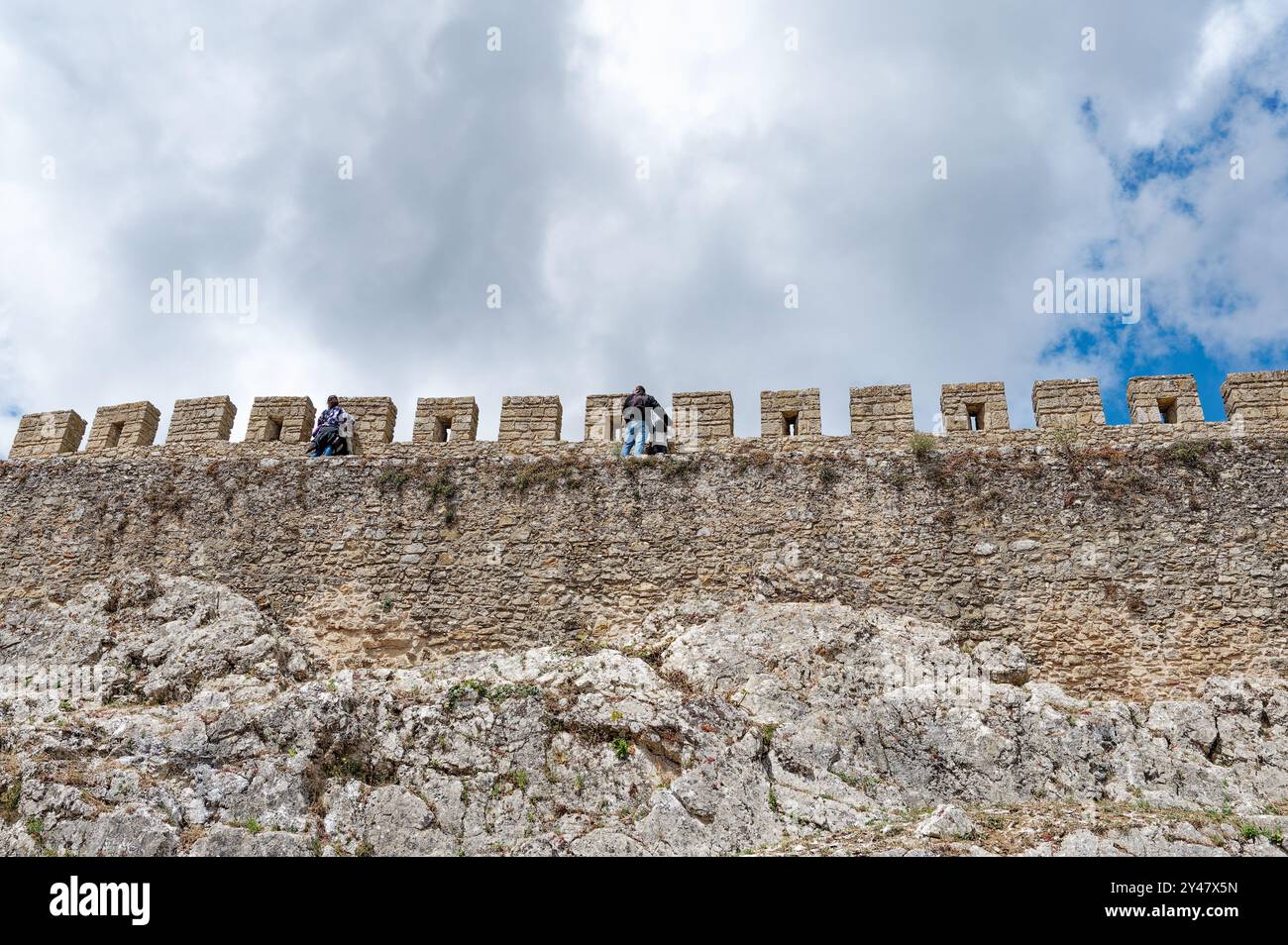 Die Reisenden besteigen die majestätischen mittelalterlichen Mauern von Óbidos, die alte Steinbefestigungen mit rauem Naturgelände unter einem dynamischen Himmel verbinden Stockfoto