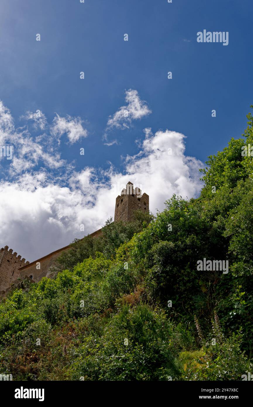 Ein hoher mittelalterlicher Turm aus der Burg Óbidos erhebt sich aus üppig grünem Laub und reicht bis zu einem tiefblauen Himmel, der von zarten Wolken verstreut ist Stockfoto