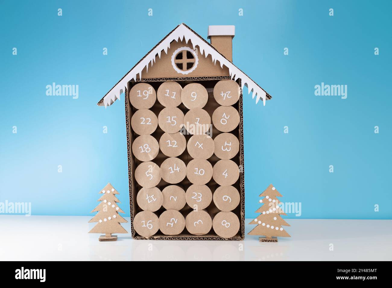 Handgefertigtes Adventskalenderhaus aus Pappe, 24 nummerierte Fächer, festliches Schneedach, Schornstein, Pappbäume, Sternenausschnitte, Weihnachtszähler, ho Stockfoto