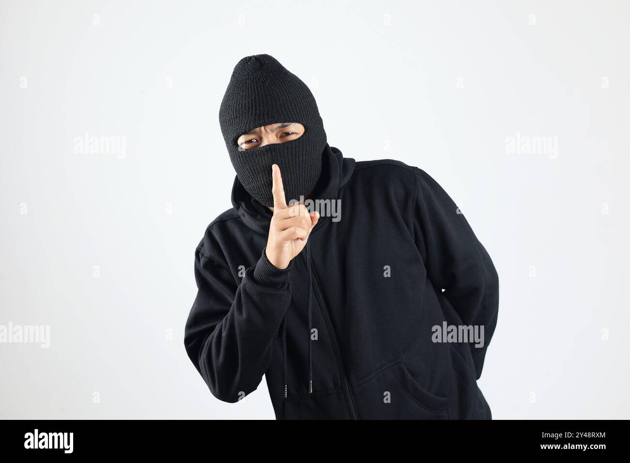Dieb in schwarzer Balaclava hält Finger auf den Lippen, macht Hush Sign, isoliert auf weißem Hintergrund Stockfoto