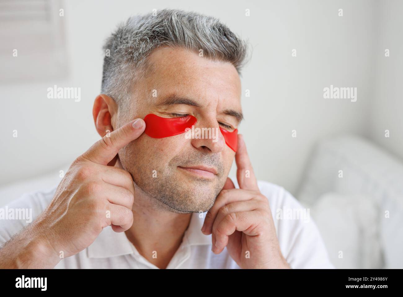 Mann, der Augenflecken auf das Gesicht aufträgt. Falten und Gesichtspflege zu Hause für Männer. Das Konzept der Gesichtsverjüngung Stockfoto