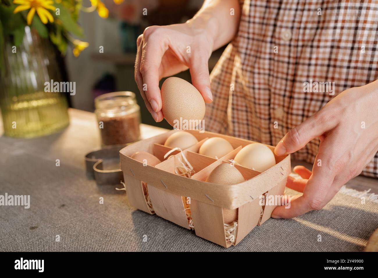 Nahaufnahme der Hand der Frau, die Ei über Korb mit mehreren Eiern hält, Küchenhintergrund. Konzept für frische Bio-Eier Stockfoto