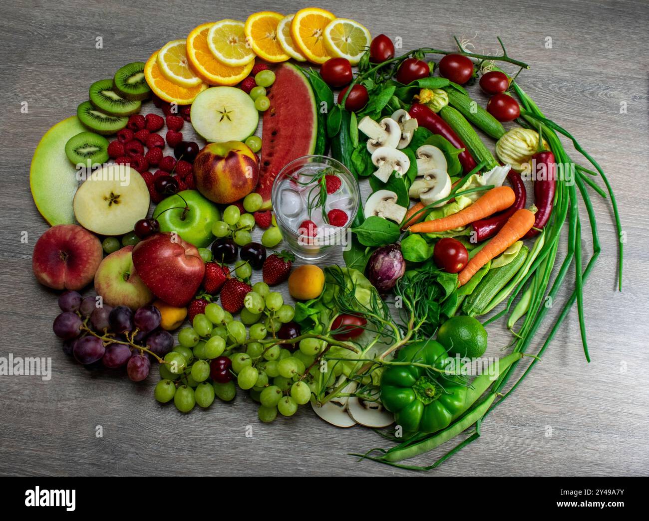 Ein Stillleben Foto mit bunten Früchten und Gemüse auf einem Tisch rund um ein Glas Wasser, das die Bedeutung einer gesunden Ernährung repräsentiert. Stockfoto