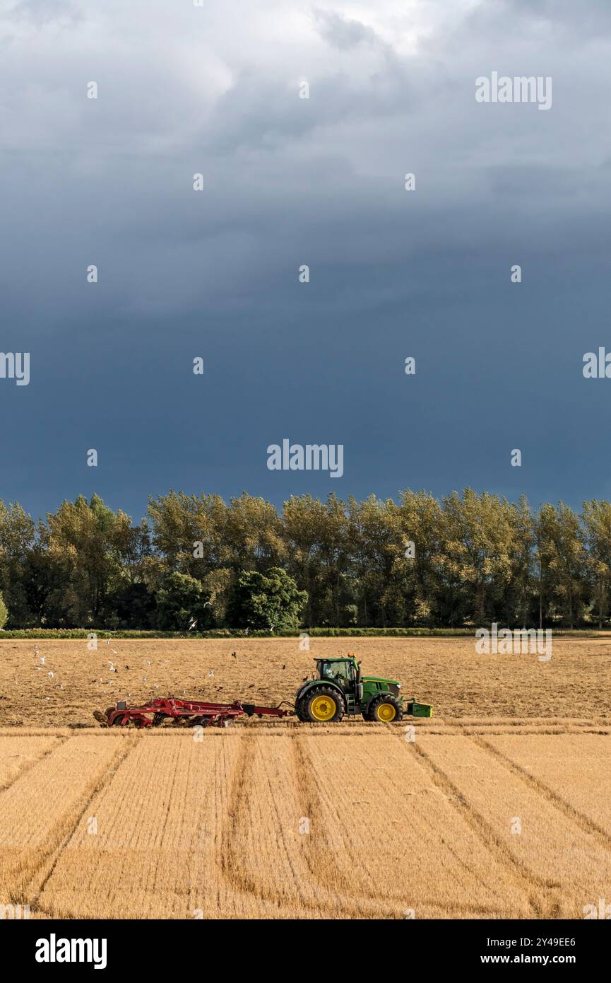 John Deere 8400R Traktor zieht einen Horsch Tiger MT Grubber vor einem dunklen stürmischen Himmel auf einem Ackerbaubetrieb in Norfolk Stockfoto