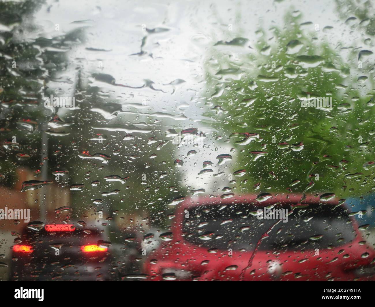 Eine enge Aufnahme eines regenbespritzten Fensters, die einen trafiktiven Autohintergrund enthüllt. Aus nächster Nähe Regentropfen am Fenster Stockfoto