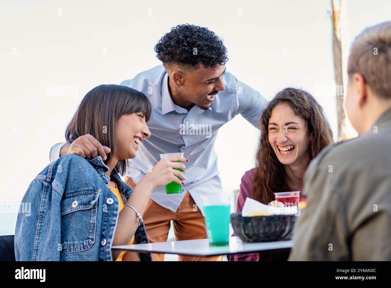 Fröhliche Interaktion zwischen verschiedenen jungen Erwachsenen, die lebendige Getränke an einem Ort am Meer genießen. Authentischer Moment der Freundschaft und Inklusivität c Stockfoto