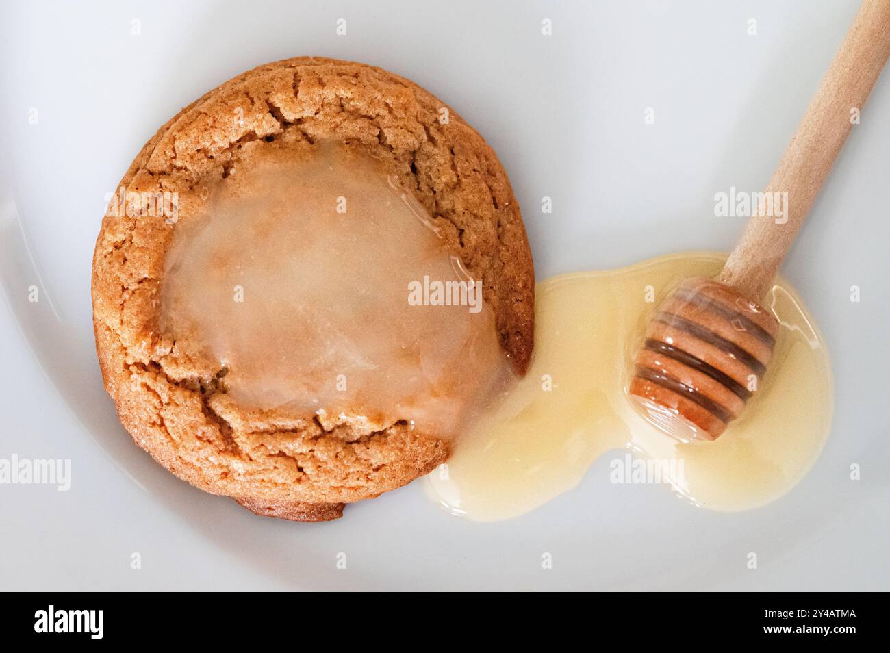 Einzelner Keks mit Honig auf weißem Teller mit Honiglöffel Stockfoto