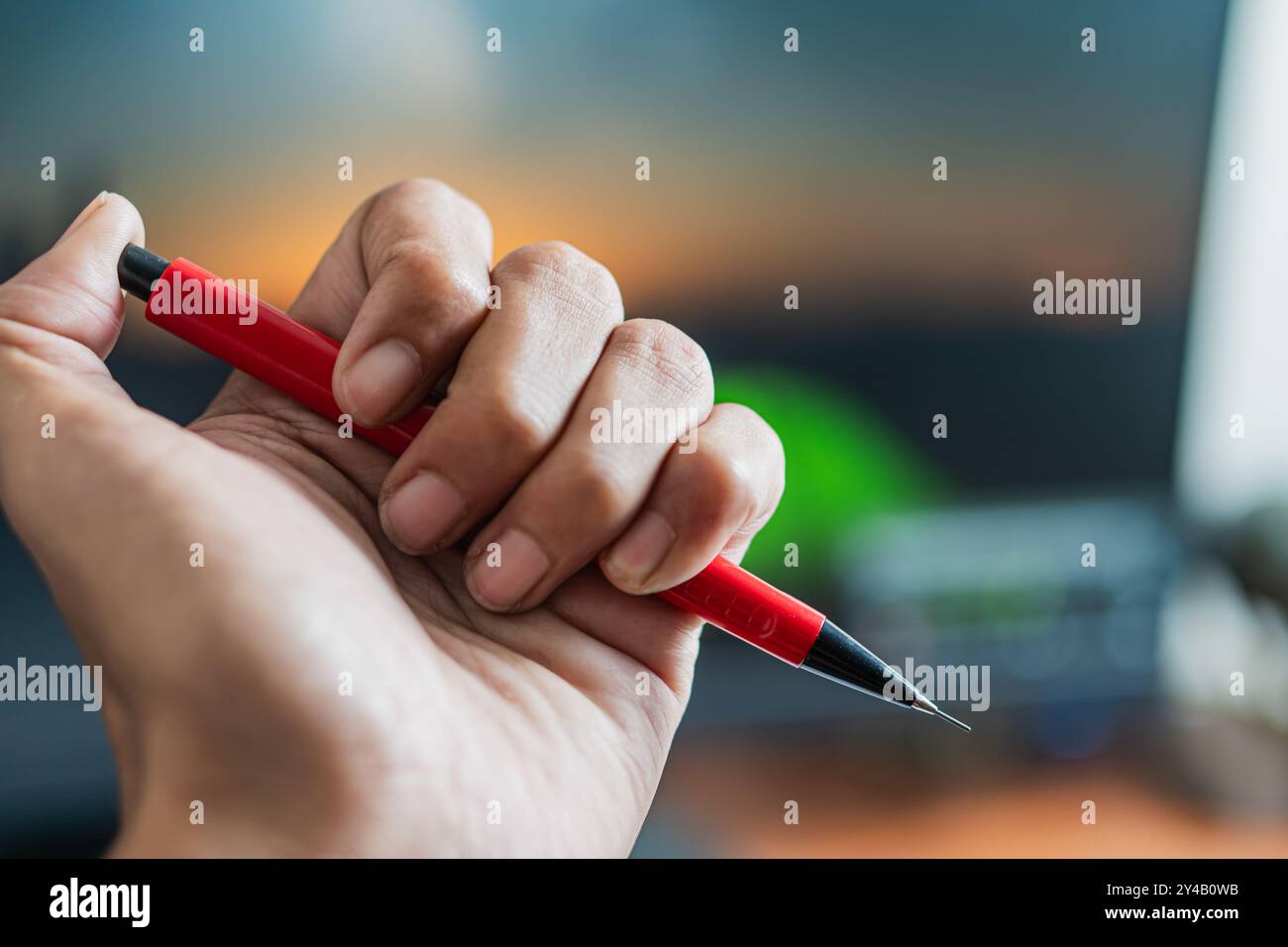 Eine Person, die einen roten Stift mit einer schwarzen Spitze vor einem hellen Hintergrund hält. Der Stift wird deutlich sichtbar angezeigt und zeigt sein Design und seine Farbe. Stockfoto