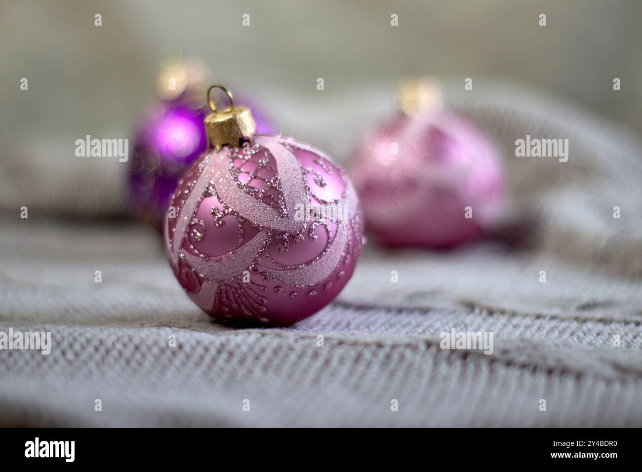 Wunderschöne lilafarbene Weihnachtskugeln mit Mustern auf einem gemütlichen hellen gestrickten Hintergrund, Nahansicht von vorne Stockfoto