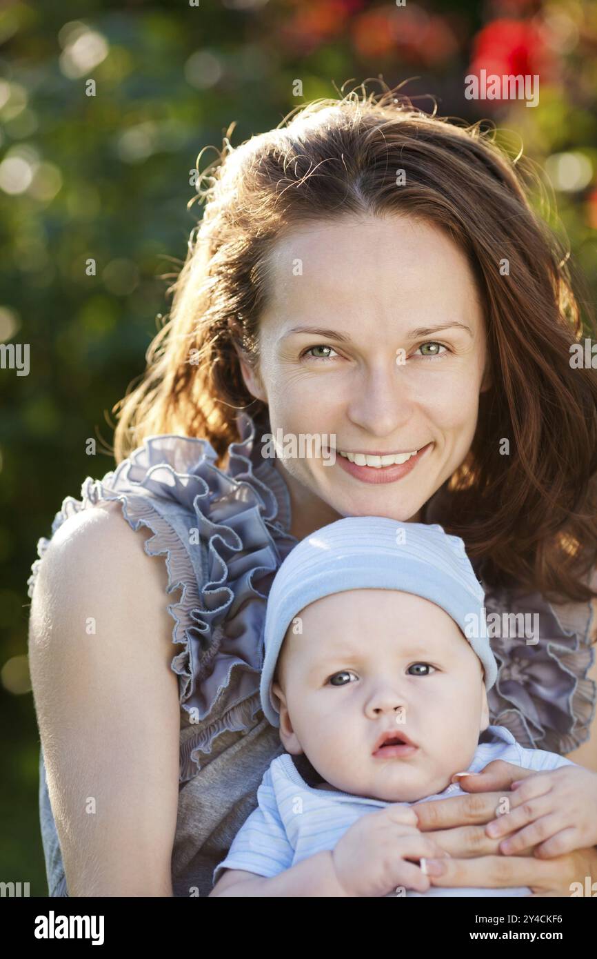 Porträt einer jungen glücklichen Frau und eines Babys in einem Garten vor einem Frühlingsblumenhintergrund Stockfoto