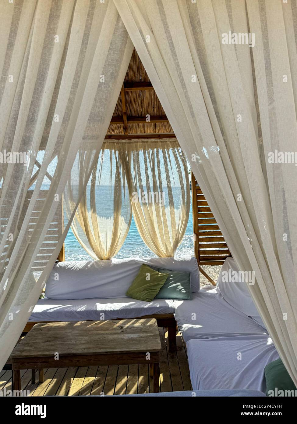 Gemütliche Strandhütte mit weißen Vorhängen und Blick auf das Meer bei Sonnenuntergang an einem ruhigen Abend Stockfoto