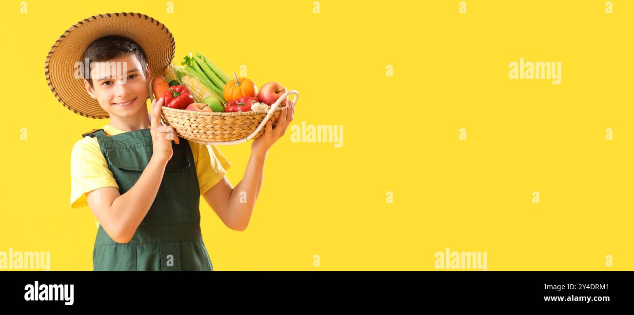 Kleiner Landwirt, der einen Korb mit frischem Gemüse und Obst auf gelbem Hintergrund mit Platz für Text hält Stockfoto