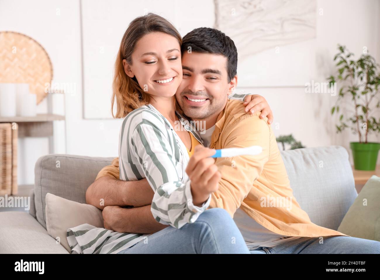 Glückliches junges Paar mit Schwangerschaftstest, das sich zu Hause umarmt Stockfoto