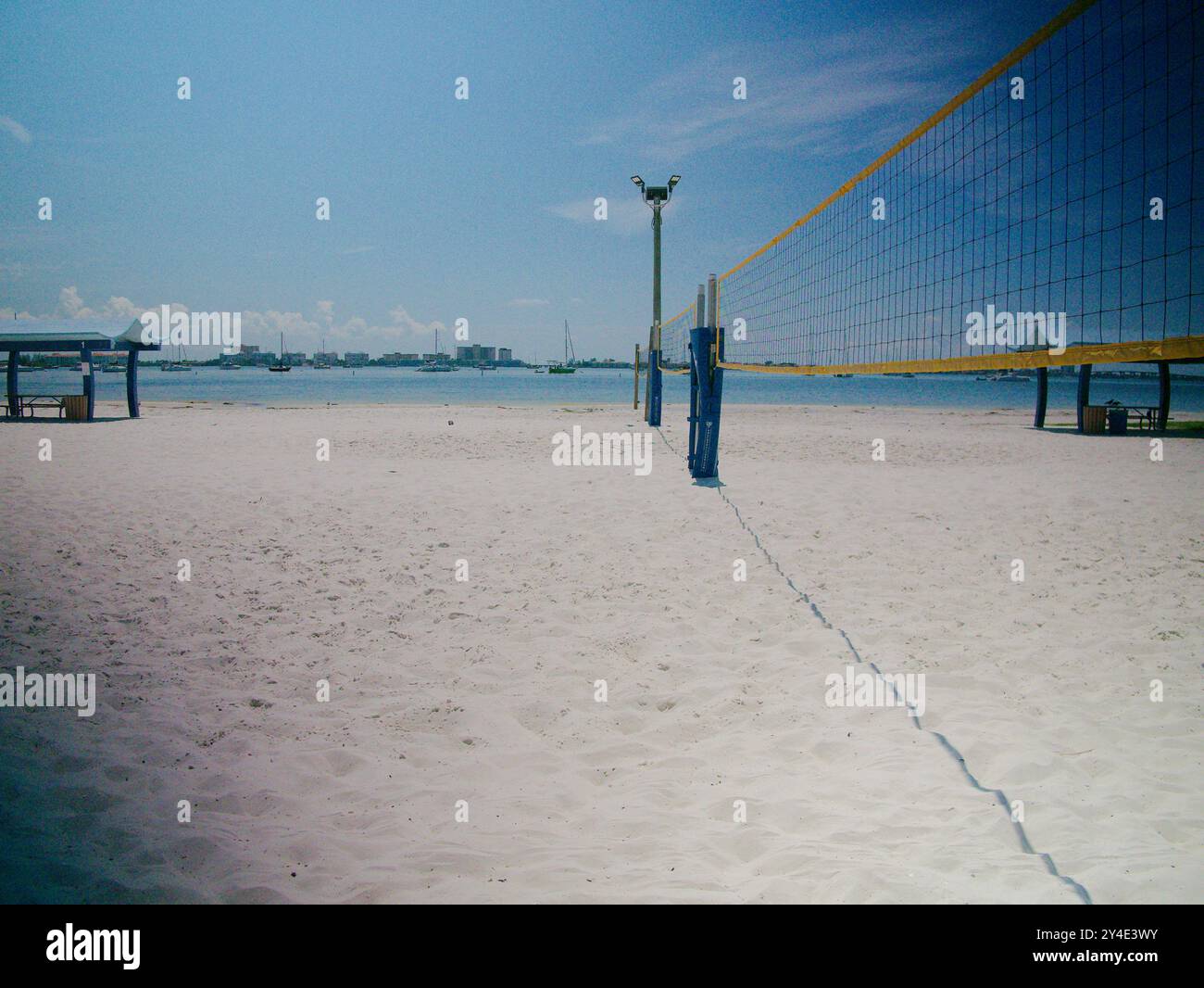 Weite Aussicht mit gelbem Rand-Volleyballnetz auf der rechten Seite mit Blick auf einen weißen Sandstrand an einem hellen sonnigen Tag in Florida. Segelboote in der Bucht Stockfoto