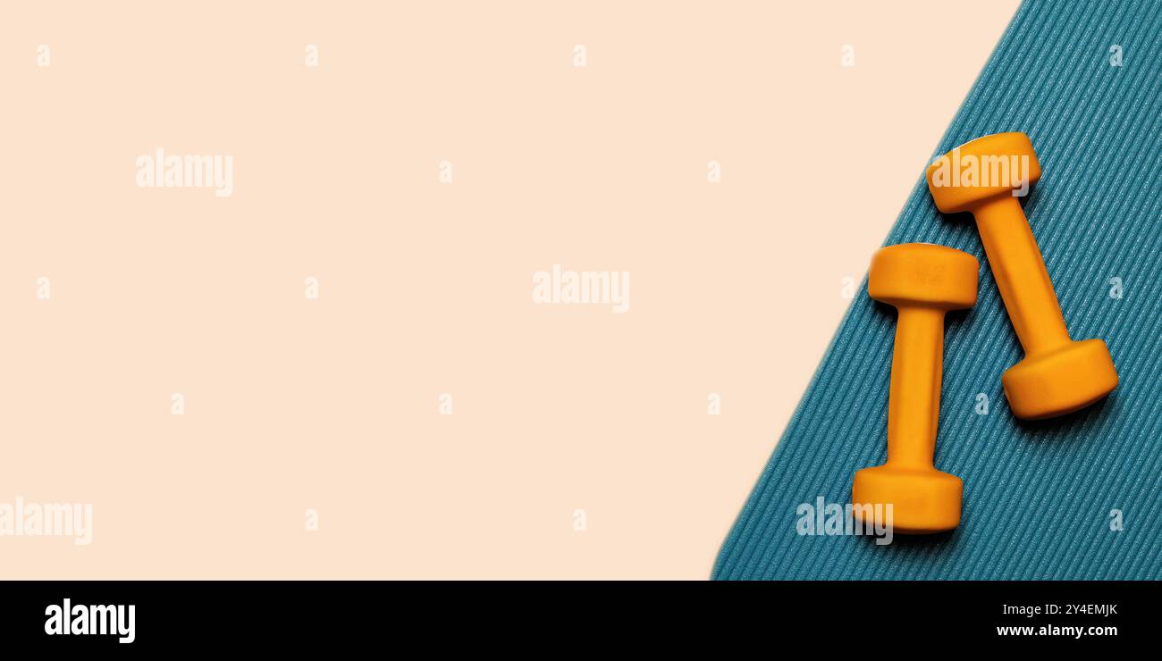 Zwei orangene Kurzhanteln liegen auf einer blauen Yogamatte. Ein großartiges Image, um Fitness, Bewegung und gesundes Leben zu repräsentieren. Bereich für Marketingvorlage kopieren Stockfoto