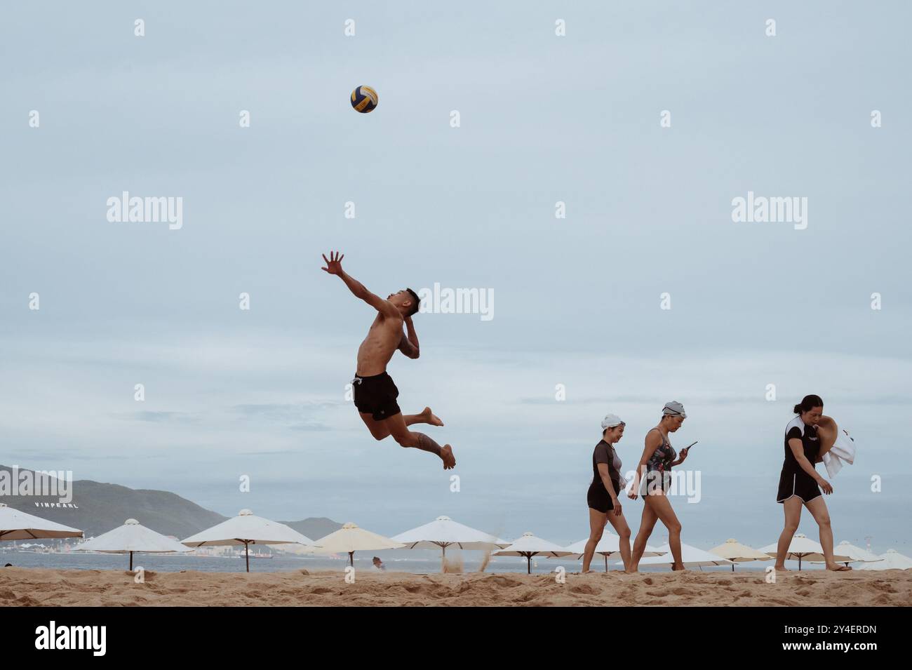 Asiatisch vietnamesischer Mann serviert den Ball bei einem Beachvolleyballspiel am Strand am Meer. Nha Trang, Vietnam - 21. Juli 2024 Stockfoto