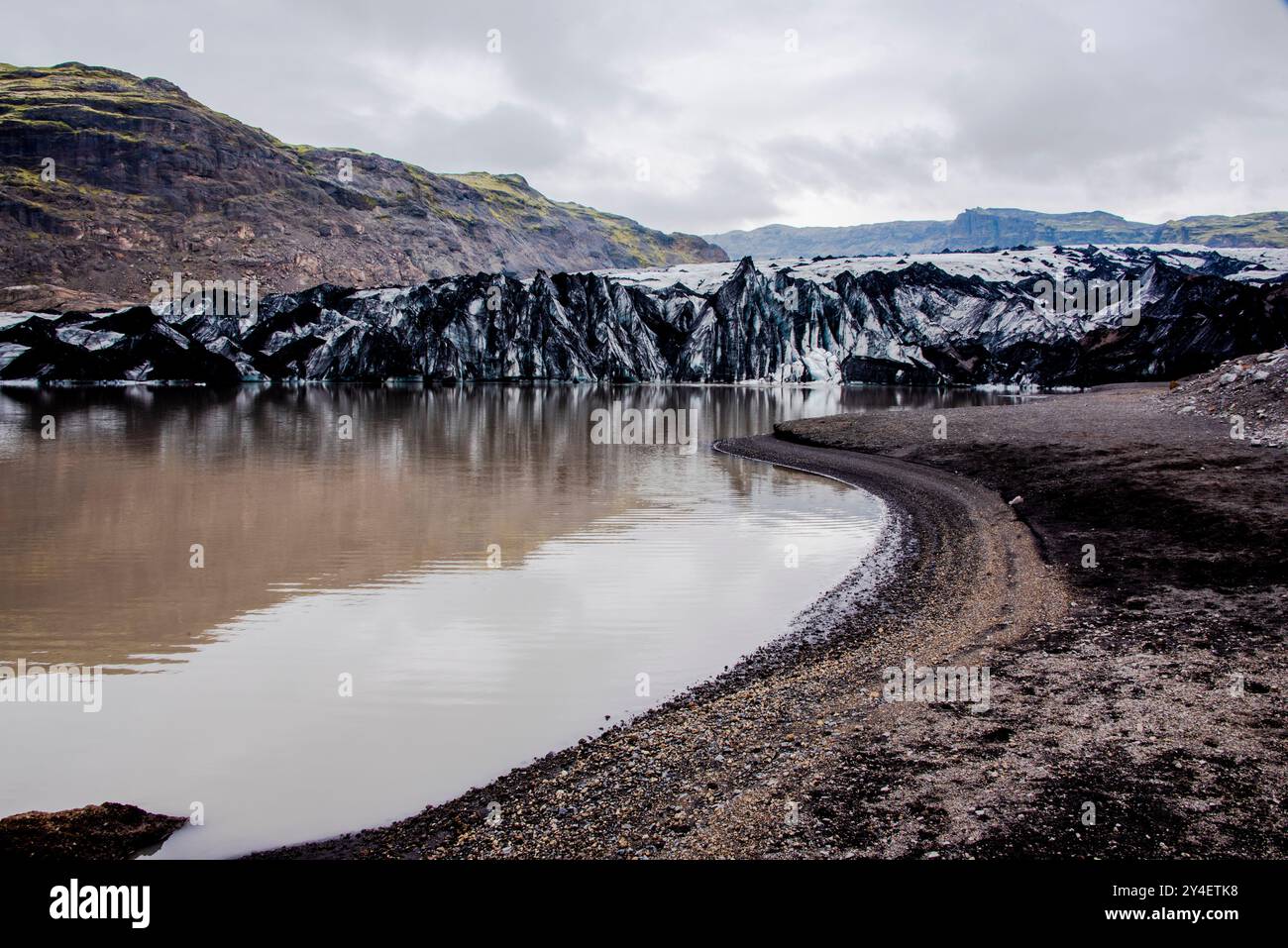 Solheimajokull-Gletscher bedeckt mit Ruß von früheren Eruptionen, wobei der Gletschersee vom Vulkan bei Vik in Island absteigt Stockfoto