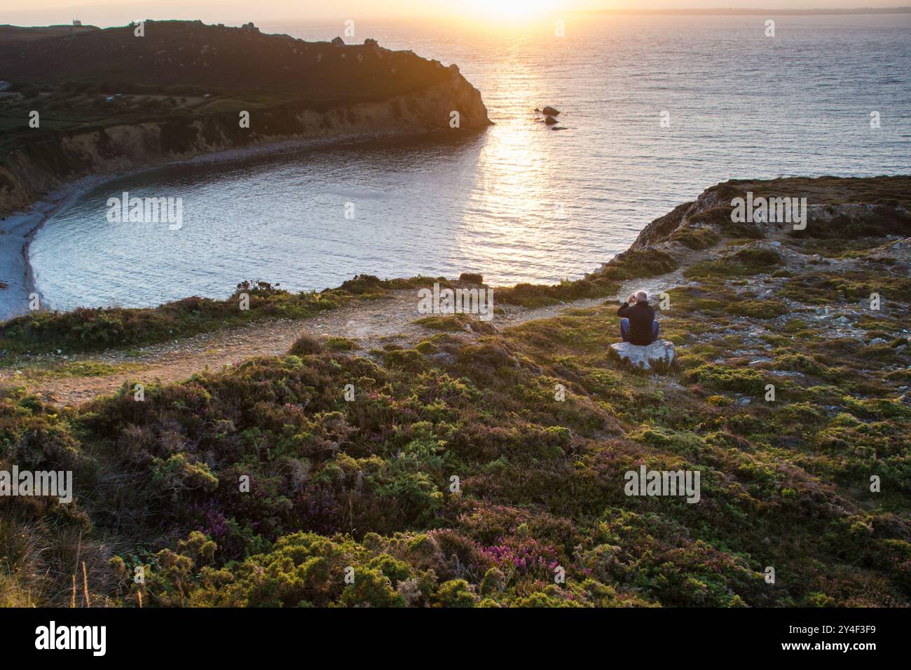 Mann, der auf der Klippe sitzt und den Sonnenuntergang in Bretagne, Frankreich, ansieht Stockfoto