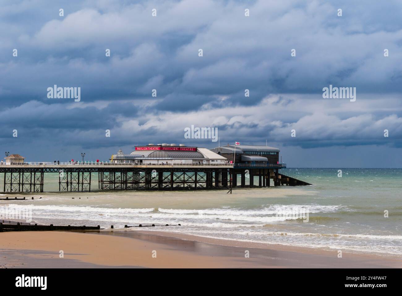 Blick vom Meer auf die RNLI Rettungsbootstaion und Pavilion Theatre am Pier unter einem dunklen bewölkten Himmel. Cromer, Norfolk, East Anglia, England, Vereinigtes Königreich, Großbritannien Stockfoto