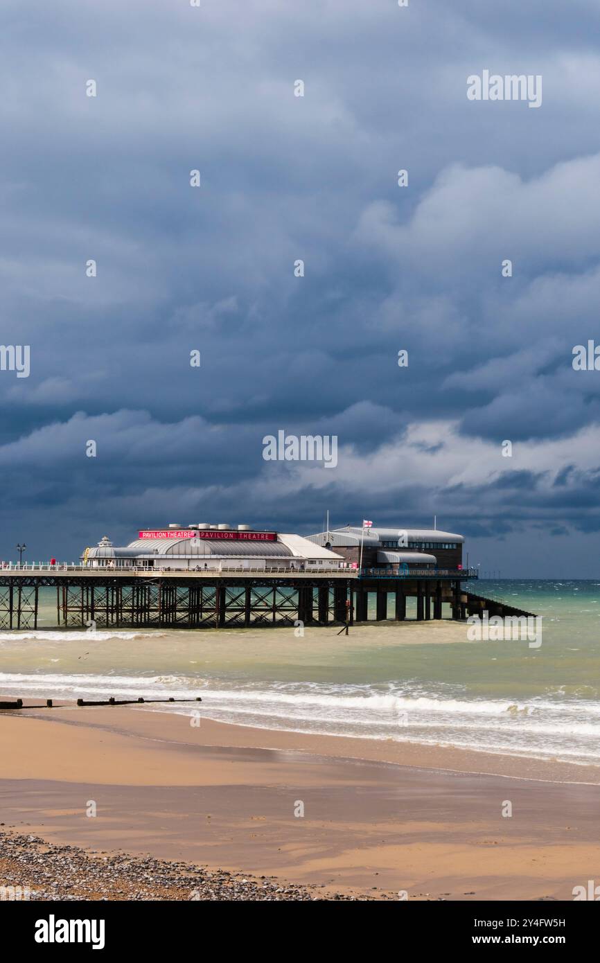 Blick vom Meer auf die RNLI Rettungsbootstaion und Pavilion Theatre am Pier unter einem dunklen bewölkten Himmel. Cromer, Norfolk, East Anglia, England, Vereinigtes Königreich, Großbritannien Stockfoto